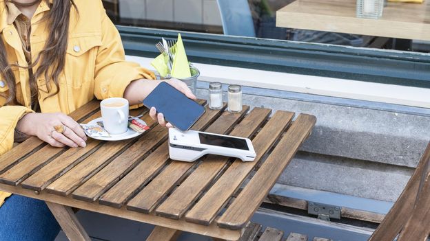 vrouw in gele regenjas houdt haar telefoon bij het pinapparaat